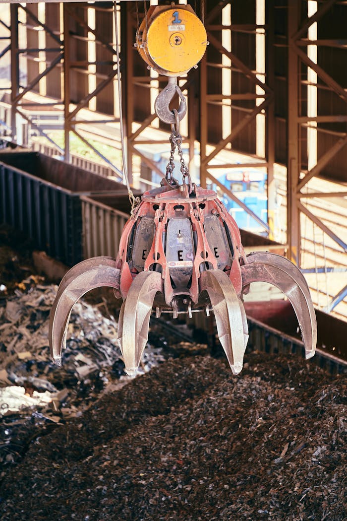 Close-up of a claw crane grasping scrap metal at a recycling plant.